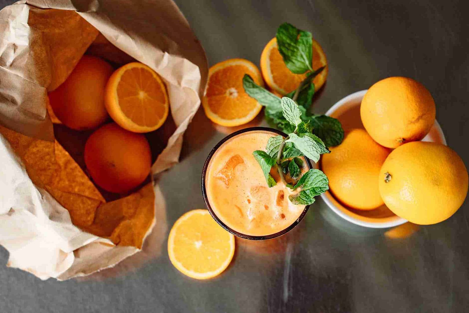 glass of orange juice with mint leaves beside oranges on metal table