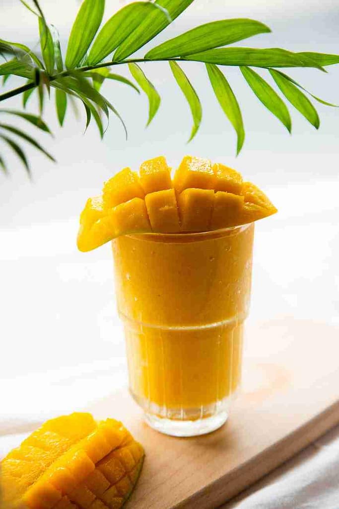 mango smoothie in clear glass topped with fresh sliced mango