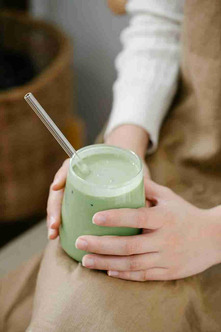 womans hands holding glass of green vegetable smoothie